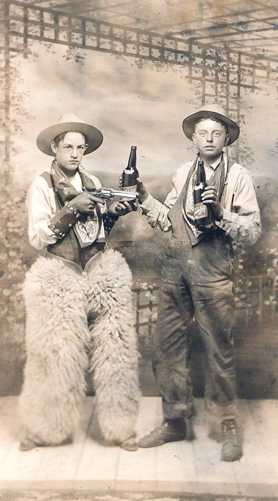 Two unidentified young men dressed in cowboy costume posing with a "six-shooter" and Schlitz beer bottles.