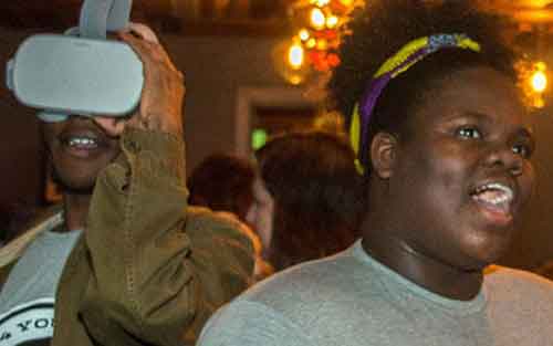 Young man using a VR headset next to a young woman talking to someone out of frame