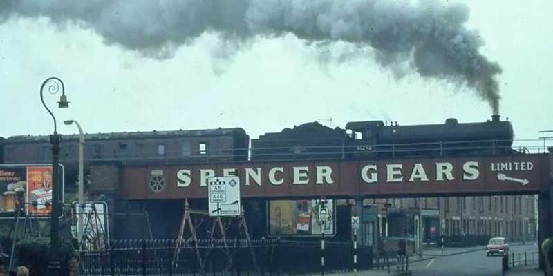 Train crossing bridge with Spencer Gears painted in all caps lettering. Circa 1970s.